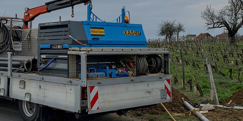 LKW mit Bohrtechnik steht am Straßenrand neben einem Weinberg, während eine Straßenbohrung durchgeführt wird.