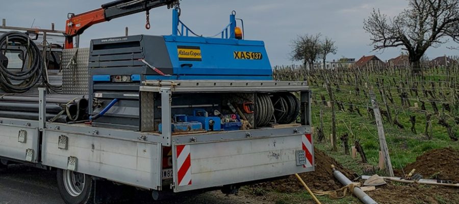 LKW mit Bohrtechnik steht am Straßenrand neben einem Weinberg, während eine Straßenbohrung durchgeführt wird.