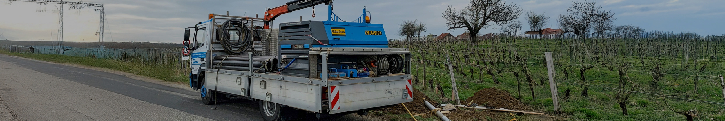 LKW mit Bohrtechnik steht am Straßenrand neben einem Weinberg, während eine Straßenbohrung durchgeführt wird.