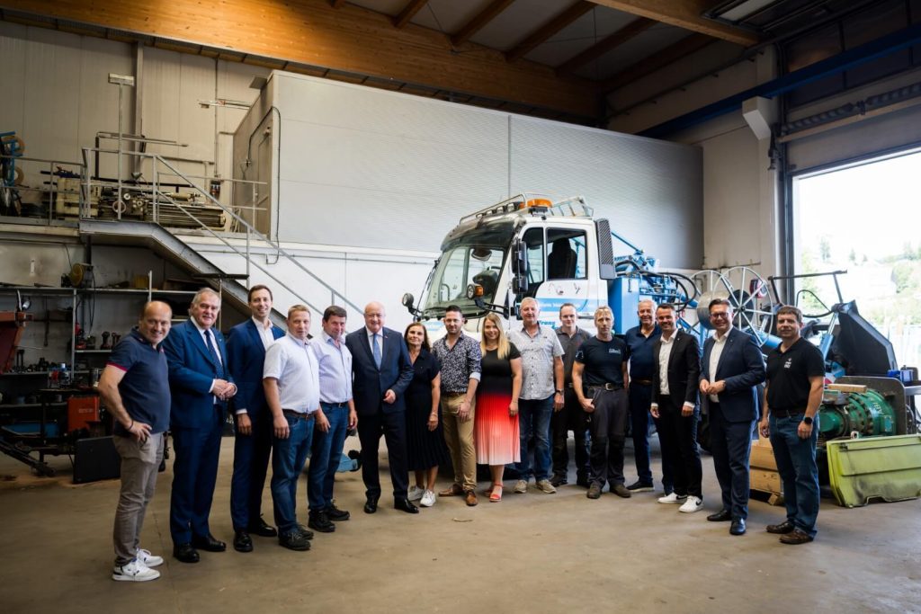 Gruppenfoto mit Kanzler Christian Stocker, dem Team der Franz Lackner GmbH und einem Spezialfahrzeug zur Kabelverlegung in der Werkstatthalle